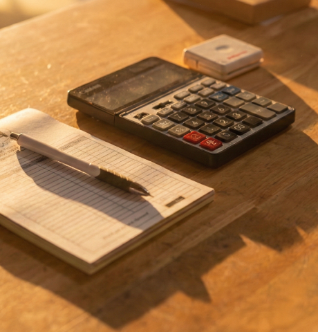 Calculator, pen, and notepad on a wooden desk, ready for inquiries when you contact Cygnus Lumber.