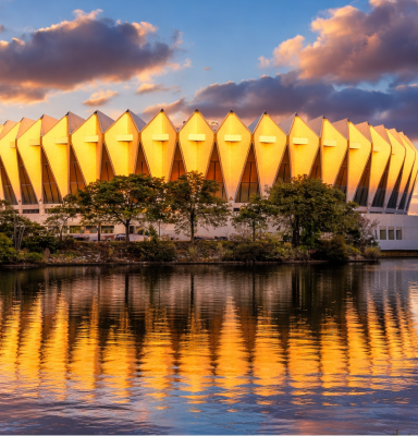 Hampton Coliseum during sunset reflecting on calm water.