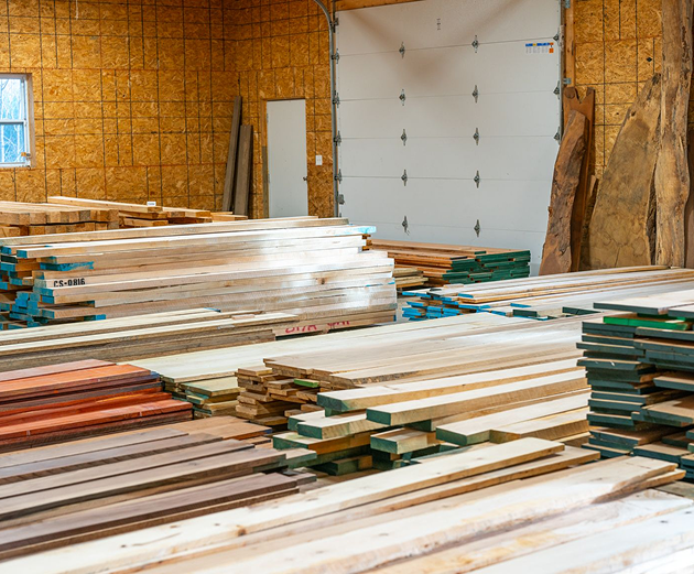 Stacks of hardwood lumber boards and live-edge slabs in a storage shop.