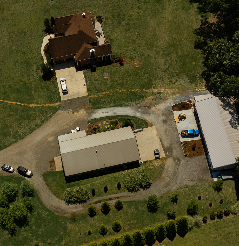 Aerial view of a rural home and workshop outbuildings on green land.