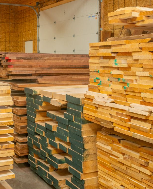 Neatly stacked timber boards with green-painted ends in a wood shop.