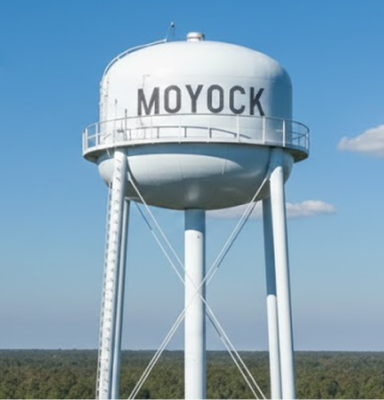Tall white Moyock water tower under a blue sky.