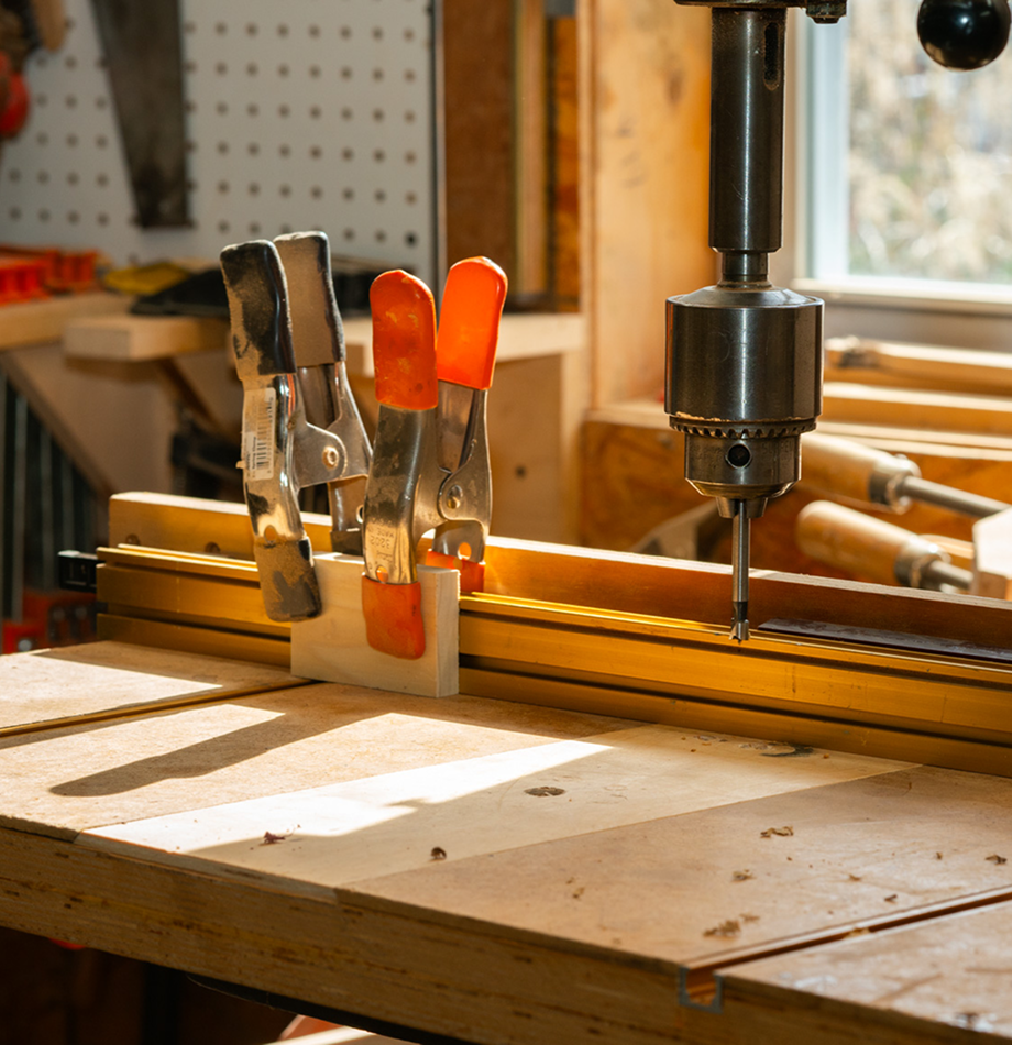 Drill press and spring clamps on a woodworking bench.