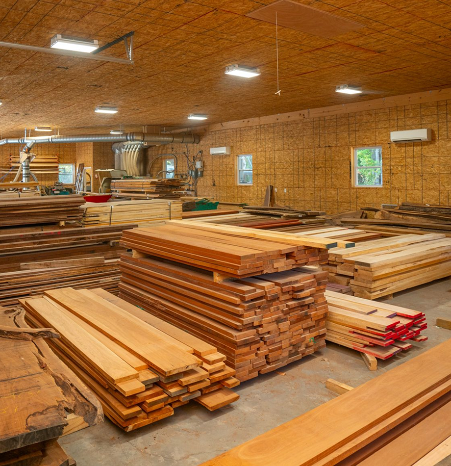 Large workshop warehouse filled with organized stacks of lumber boards.