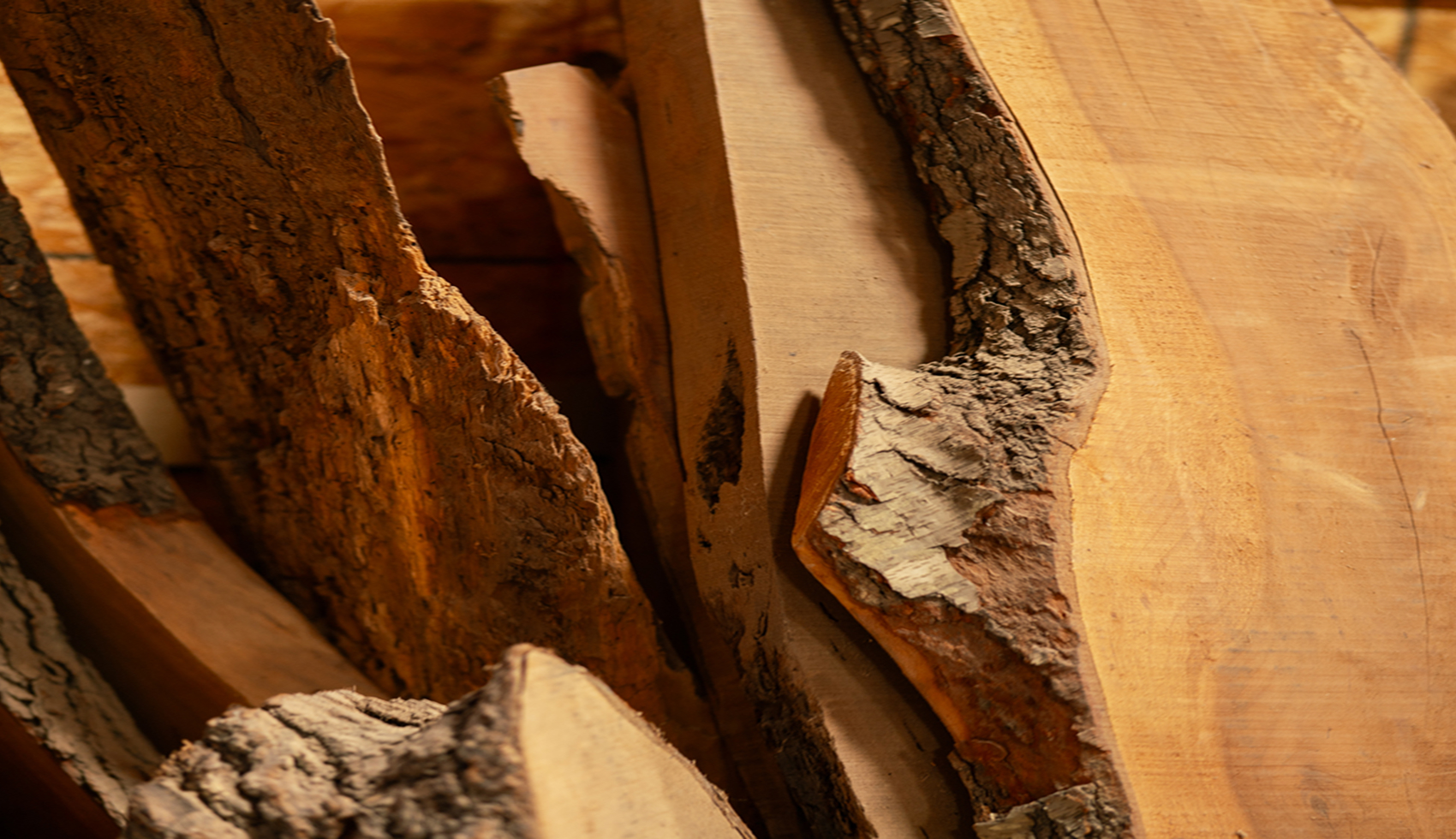 Close-up of natural live-edge raw wood slabs with bark inside a lumber yard.