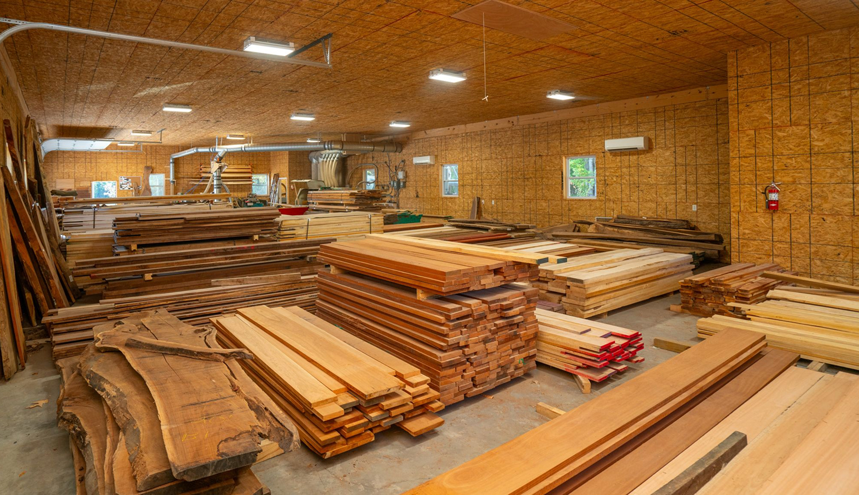 Organized stacks of various lumber and live-edge wood slabs inside a warehouse.